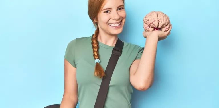 Mujer joven con bolsa de entrenamiento sostiene un cerebro de plástico sonriendo