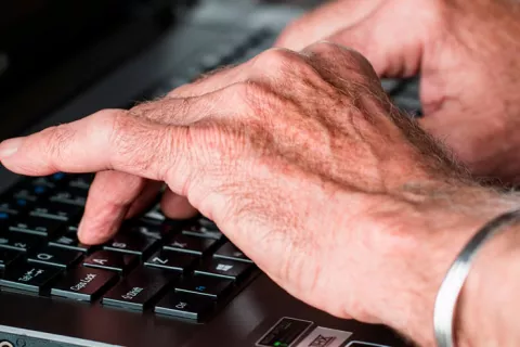 Persona mayor escribiendo en un teclado de ordenador