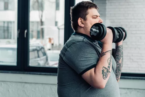 El entrenamiento de fuerza, efectivo para reducir la grasa del corazón Hombre con obesidad realizando ejercicio con pesas para reducir la grasa del corazón