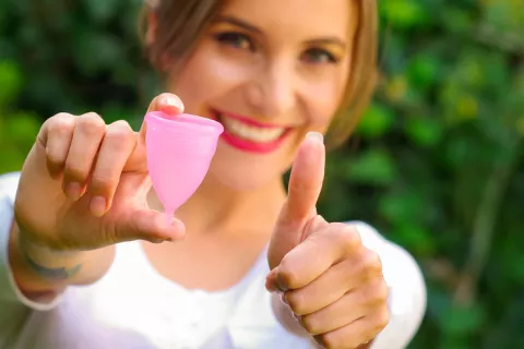 Una mujer con el pulgar hacia arriba mostrando una copa menstrual