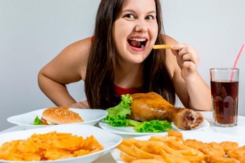 Mujer joven cenando multitud de alimentos grasos