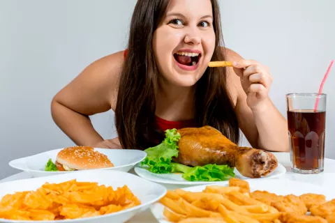 Mujer joven cenando multitud de alimentos grasos