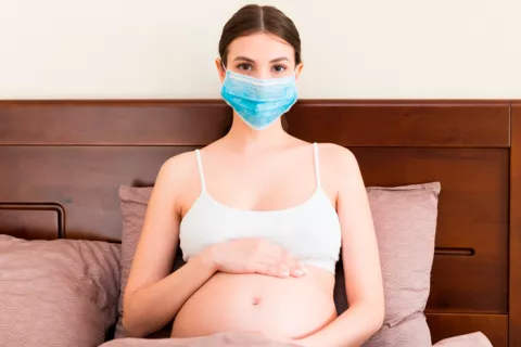 Menos síntomas, pero más riesgo de gravedad Embarazada en la cama con una mascarilla anti-covid-19