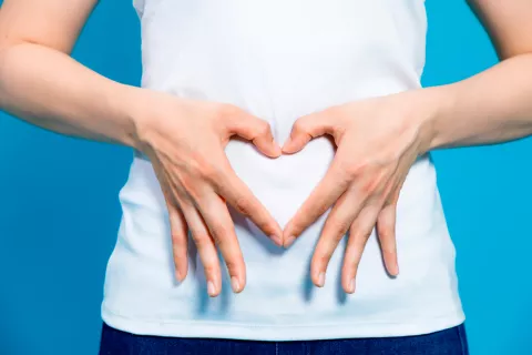 Mujer formando un corazón con las manos a la altura del abdomen