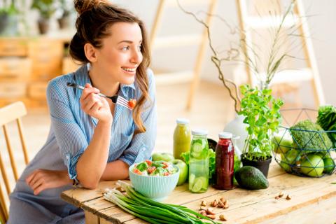 Mujer joven comiendo ensalada con ingredientes frescos verdes