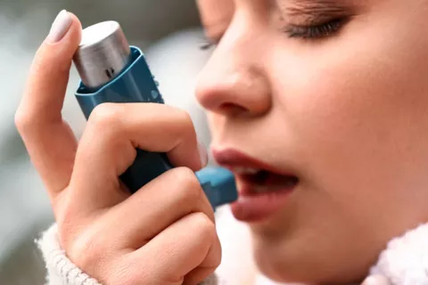 Mujer joven inhalando un corticoide para el asma