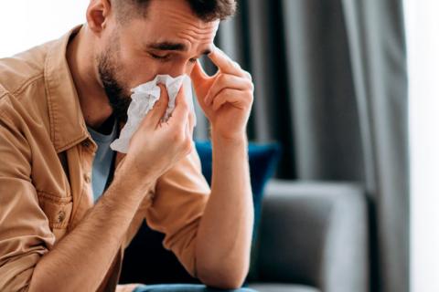 Hombre joven enfermo por coronavirus sonándose la nariz con un pañuelo