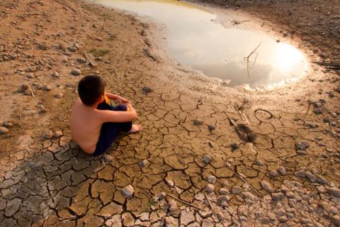 Niño sentado en tierra agrietada junto a una laguna seca