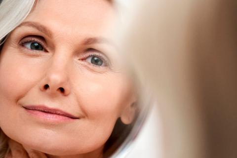 Mujer mayor mirando al espejo la piel sin arrugas de su rostro