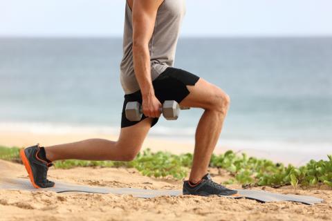 Un hombre hace ejercicio en la playa con pesas