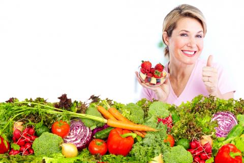 Mujer de mediana edad sonríe tras amplia variedad de frutas y verduras