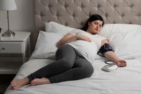 Mujer embarazada tumbada en su cama se mide la presión arterial
