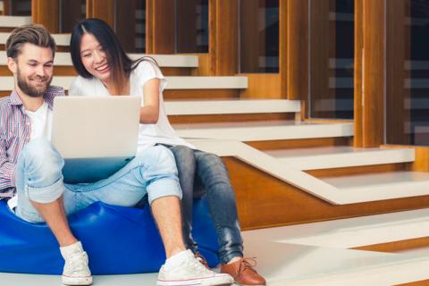 Dos universitarios sentados en las escaleras de la facultad mirando su dispositivo electrónico