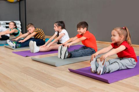 Niños pequeños sentados en el suelo haciendo ejercicio físico en el gimnasio de la escuela