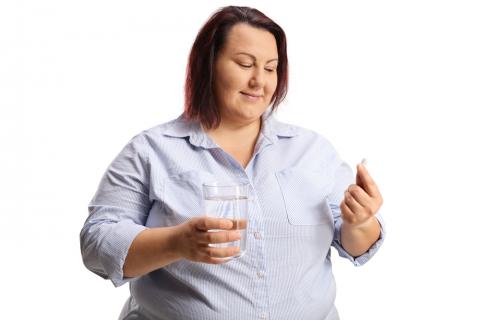 Mujer obesa sostiene un vaso de agua y una píldora