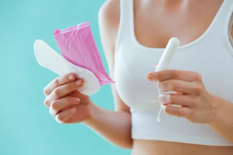 Mujer joven sostiene en sus manos un tampón, una compresa y un salvaslip