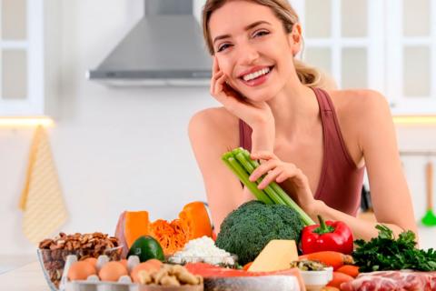 Mujer sonriendo y sentada en una mesa con alimentos sanos