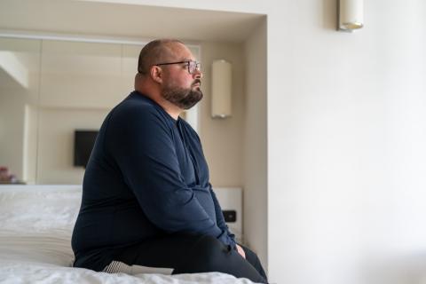 Hombre triste y obeso sentado en la cama y mirando por la ventana