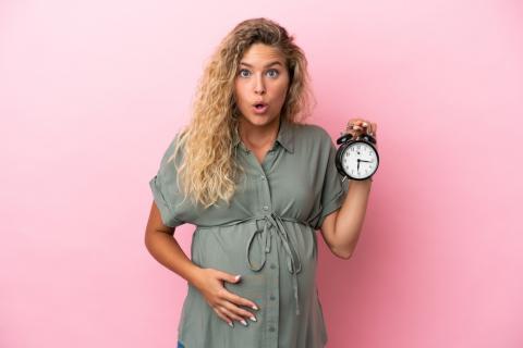 Mujer rubia embarazada con cara de sorpresa y un reloj en la mano