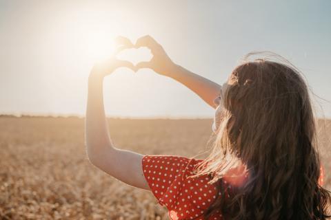 Woman facing the sun making a heart gesture with her hands