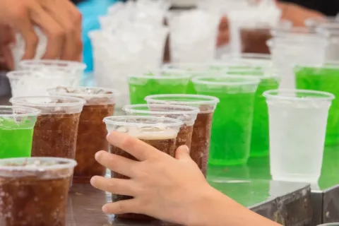 Mano de un niño coge una de las muchas bebidas azucaradas que hay sobre una mesa