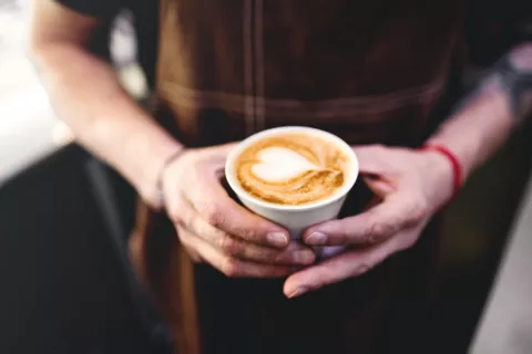Hombre sostiene una taza de café con un corazón dibujado en la espuma
