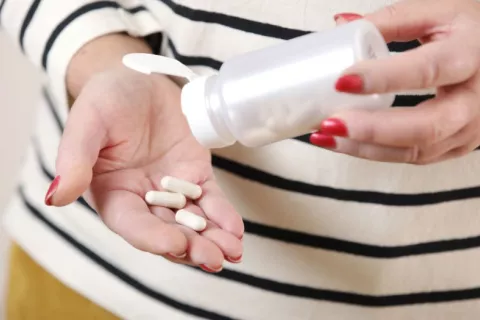 Una pastilla oral para bajar el colesterol reduce problemas cardiovasculares en pacientes de riesgo Mano de mujer con unas píldoras que han salido de un bote abierto en su otra mano