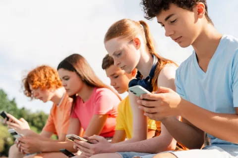 Adolescentes usando redes sociales expuestos a mala salud mental Grupo de adolescentes sentados al aire libre absortos en sus teléfonos móviles