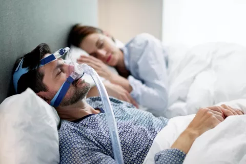 Hombre con mascarilla nasal CPAP para tratar la apnea del sueño Hombre joven con dispositivo CPAP duerme junto a su pareja