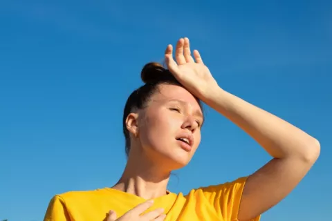 El calor afecta negativamente a una mujer Mujer joven bajo el sol se toca el pecho y la frente con gesto de agobio