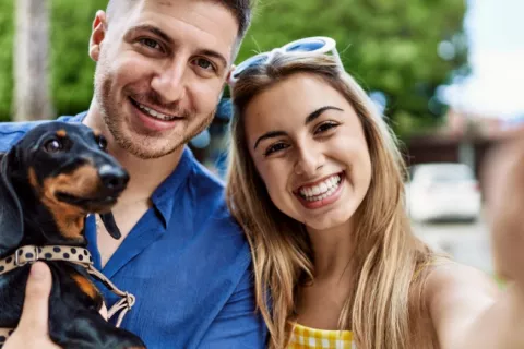 Perro pequeño en brazos de su dueño mira a la cámara del móvil Una joven pareja con su perro en brazos se hace un selfie
