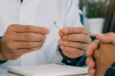 Médico aconseja a un paciente dejar de fumar y rompe un cigarrillo Un médico rompe un cigarrillo frente a un paciente
