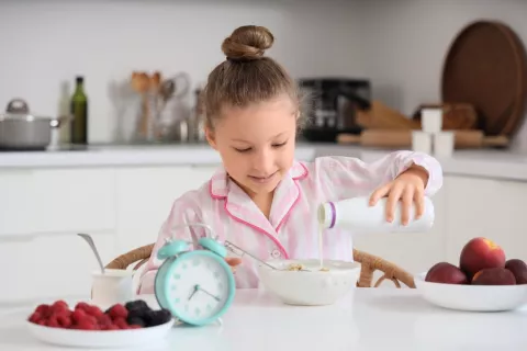 Hora del desayuno de los niños Niña en pijama se sirve leche en los cereales con un reloj que marca las 7 de la mañana