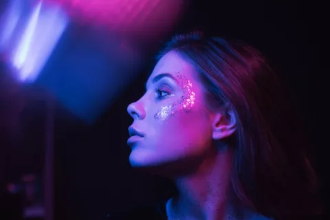 Morena con maquillaje brillante de prupurina en la cara en una habitación oscura