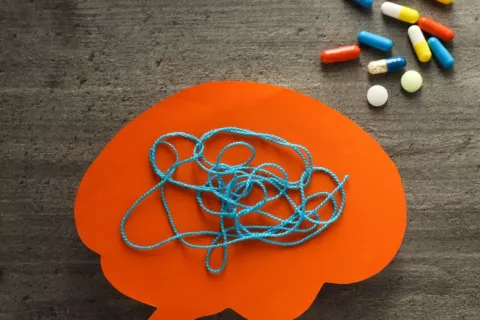 Medicamentos para tratar la esquizofrenia junto a un cerebro de papel con hilo enredado Cerebro de papel con hilo enredado junto a diversos medicamentos