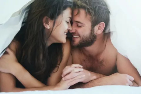 Complicidad de una mujer y un hombre bajo el edredón de su cama Hombre y mujer se sonríen con complicidad bajo el edredón de su cama