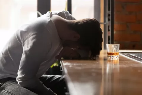 Joven alcohólico en el bar con un vaso de wisky Joven ebrio apoya su cabeza sobre la barra del bar junto a un vaso de wisky