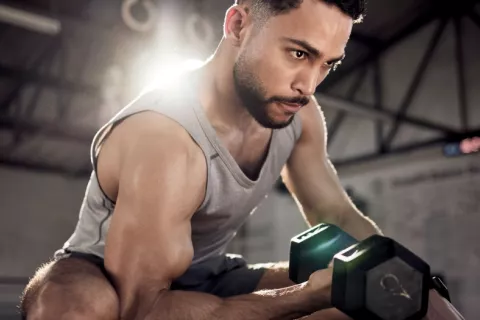 Hombre levanta pesas para ganar músculo Hombre joven musculado entrena con mancuernas en un gimnasio