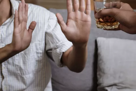 Hombre rechaza un vaso con whisky Un hombre muestra las palmas de sus manos para rechazar el vaso con whisky que otro le ofrece