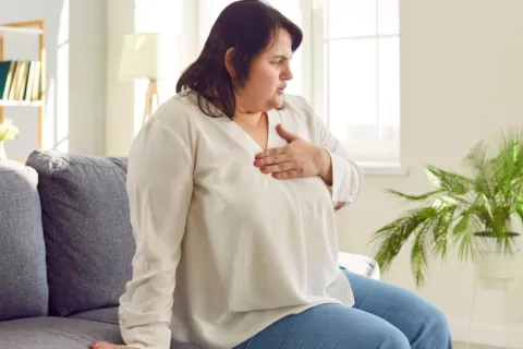 Mujer con sobrepeso con síntomas de infarto de miocardio Mujer obesa sentada en su casa se toca el pecho con gesto de dolor