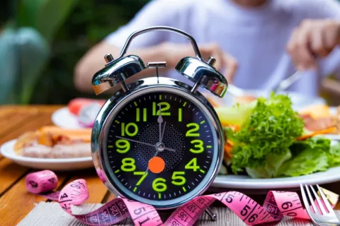 Ayuno intermitente versus restricción calórica para perder peso Persona se dispone a comer con un reloj y una cinta métrica en primer plano