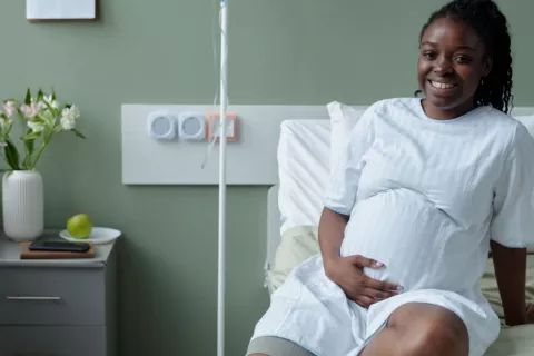 Joven embarazada en el hospital para un control prenatal Sonriente joven negra embarazada sentada sobre la cama del hospital