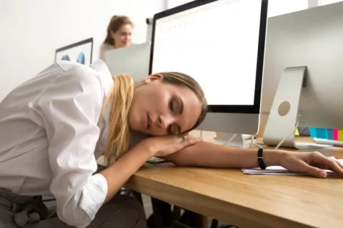 Joven mujer con fatiga crónica descansa sobre su mesa de trabajo Mujer joven en su mesa de trabajo con la cabeza apoyada sobre un brazo y los ojos cerrados