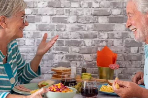 Pareja de adultos mayores disfruta de su comida sin contar calorías Mujer y hombre mayores charlan sonrientes mientras disfrutan de su comida