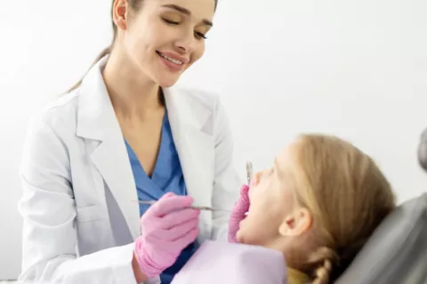 Niña pequeña con caries en el dentista Una joven dentista revisa la boca a una niña pequeña
