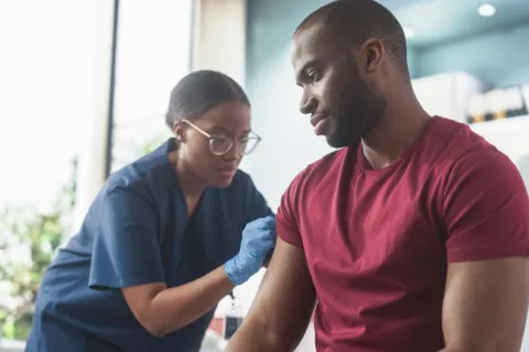 Sanitaria vacuna a hombre joven africano en un centro médico