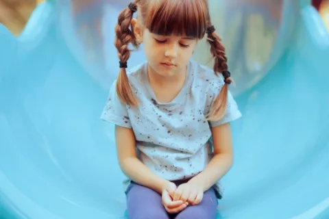 Niña triste y sin ganas de jugar sentada en el patio de recreo Niña pequeña sentada con expresión triste