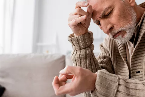 Hombre con síntomas de párkinson en el lado izquierdo hombre de pelo gris con síndrome de parkinson y temblor en las manos sentados con los ojos cerrados en el sofá en casa