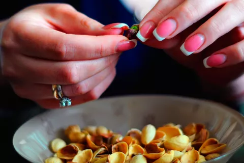 Beneficios del consumo de pistachos para la salud Manos de mujer con uñas pintadas pelan pistachos