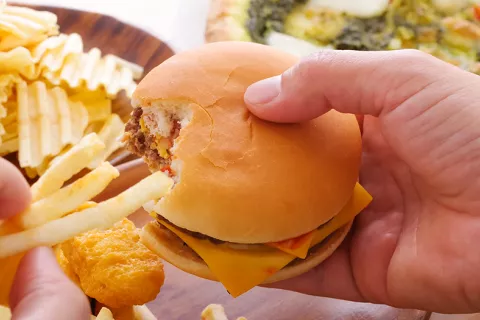 Hamburguesa y patatas fritas, como menú típico ultraprocesado Manos sostienen una hamburguesa y unas patatas fritas